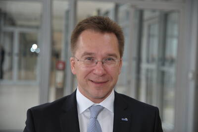 Mittelalterlicher Mann mit Brille im Anzug lächelt in einem modernen, hellen Büroflur in die Kamera