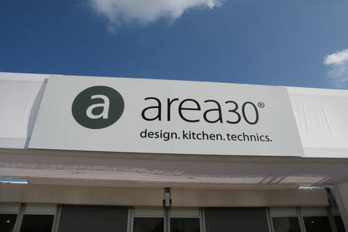 Großes weißes Messeschild mit dem Schriftzug „area30 – design.kitchen.technics.“ vor blauem Himmel