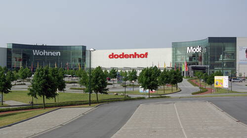 Großes dodenhof-Einkaufszentrum mit den Bereichen Wohnen und Mode, umgeben von Bäumen, Fahnen und einem weitläufigen Parkplatz im Vordergrund