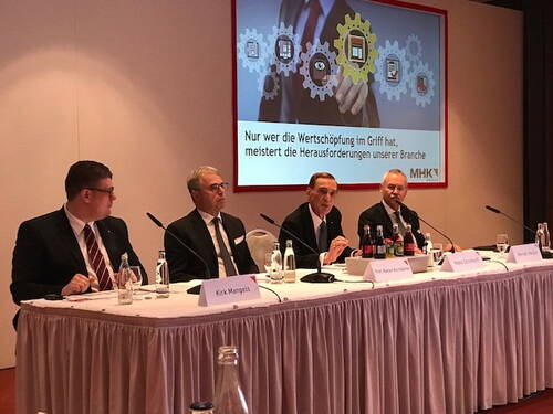 Vier Manager diskutieren auf einem Podium vor einer Präsentationsfolie zum Thema Wertschöpfung und Branchenherausforderungen bei einer MHK-Konferenz