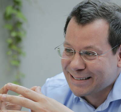 Lächelnder Mann mit Brille in hellem Hemd, der gestikulierend in ein Gespräch vertieft ist.