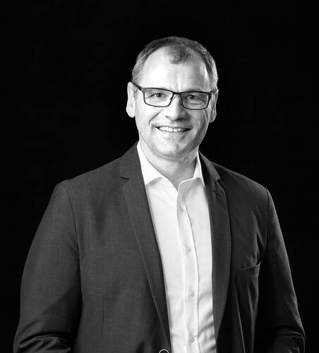 Lächelnder Mann mit Brille im Anzug vor schwarzem Hintergrund in klassischem Schwarz-Weiß-Porträt