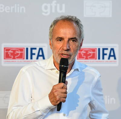 Älterer Mann im weißen Hemd spricht mit Mikrofon vor einer IFA-Pressewand in Berlin