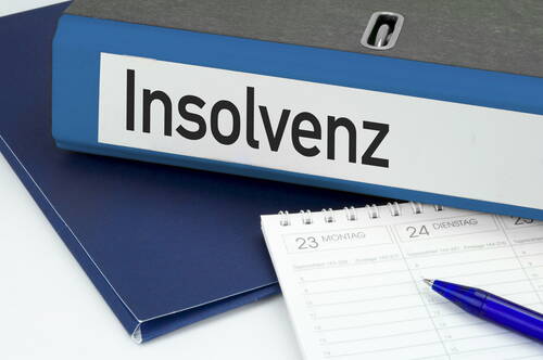 Aktenordner mit der Aufschrift „Insolvenz“ liegt auf Unterlagen neben aufgeschlagenem Terminkalender und blauem Kugelschreiber