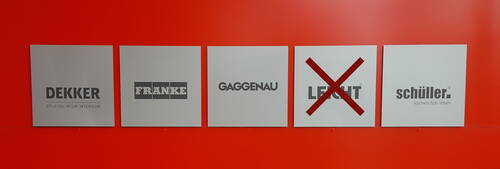 Fünf nebeneinander angeordnete Herstellerlogos auf grauen Tafeln vor roter Wand, wobei das Logo „LEICHT“ mit einem großen roten Kreuz durchgestrichen ist.