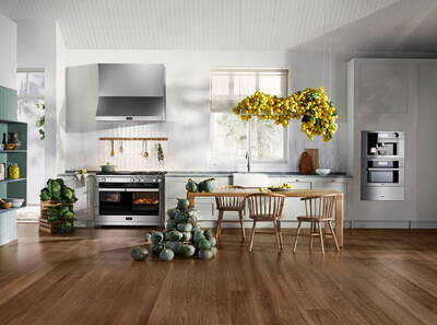 Modern helle Landhausküche mit Holzboden, großem Holztisch, gestapelten grünen Kürbissen und einer üppigen, über der Arbeitsplatte schwebenden Dekoration aus gelben Zitronen.