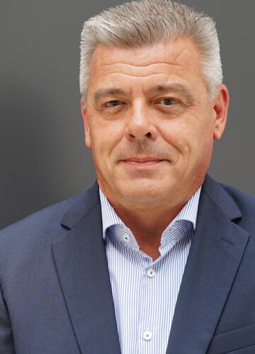 Geschäftsmann mittleren Alters im blauen Anzug mit gestreiftem Hemd blickt ernst in die Kamera vor neutral grauem Hintergrund