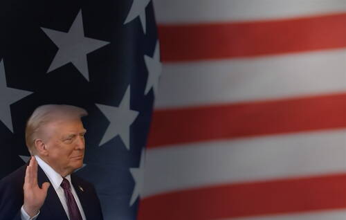 Mann im Anzug hebt die rechte Hand zum Schwur vor einer großformatigen US-Flagge im Hintergrund