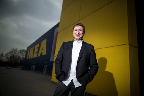 Lächelnder Mann im Anzug steht mit den Händen in den Taschen vor der gelb-blauen Fassade eines IKEA-Einrichtungshauses
