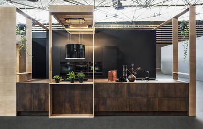 Moderne Kochinsel aus dunklem Holz mit hängender Dunstabzugshaube, Kräutertöpfen und Deko-Vasen in einer offen gestalteten Designküche vor schwarzer Rückwand