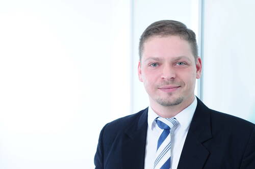 Geschäftsmann im Anzug mit gestreifter Krawatte lächelt leicht vor hellem, modernem Bürohintergrund