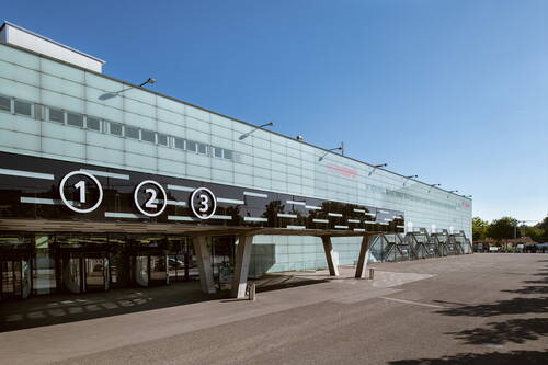 Moderne Messehalle BERNEXPO mit verglaster Fassade, nummerierten Eingängen 1, 2 und 3 und leerem Vorplatz unter blauem Himmel