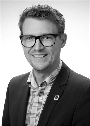 Lächelnder Mann mit Brille im Anzug und kariertem Hemd vor hellem Hintergrund in einem professionellen Porträtfoto