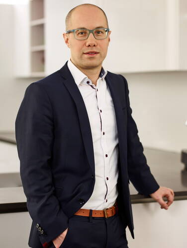 Geschäftsmann mit Glatze und Brille steht im modernen Büro an einer Theke und schaut direkt in die Kamera
