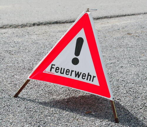 Dreieckiges Warnschild mit rotem Rand und Ausrufezeichen, das auf die Feuerwehr und einen möglichen Einsatz auf der Straße hinweist