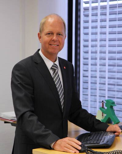 Geschäftsmann im Anzug steht lächelnd an einem Schreibtisch im Büro und bedient eine Computertastatur neben einem grünen Ampelmännchen-Dekorationsobjekt