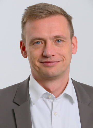 Mittelalter Mann im grauen Sakko und weißem Hemd lächelt leicht vor neutralem, hellgrauem Hintergrund