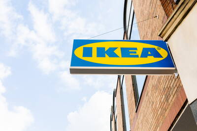 Leuchtendes blau-gelbes IKEA-Firmenschild ragt an einer Ziegelhausfassade in den hellen Himmel