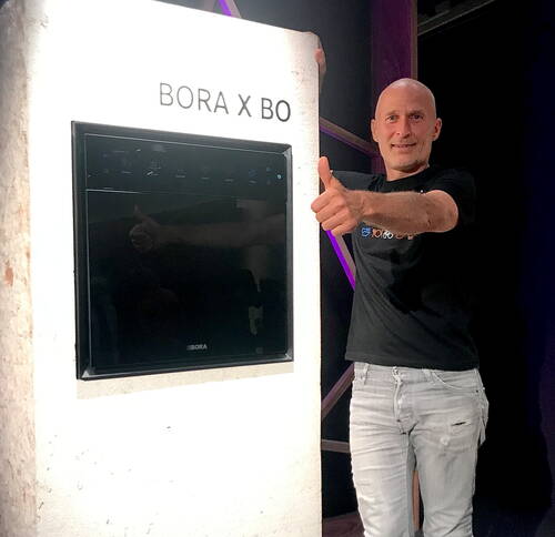 Mann steht neben einem in eine weiße Wand integrierten BORA X BO Ofen und zeigt mit erhobenem Daumen seine Zufriedenheit mit dem Gerät