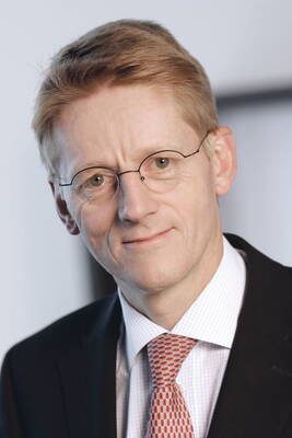 Mittelalterlicher Mann mit kurzen hellbraunen Haaren, Brille und Anzug mit rot gemusterter Krawatte blickt freundlich in die Kamera vor neutralem Hintergrund.