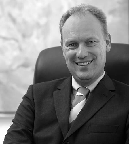 Lächelnder Mann im Anzug sitzt in einem Bürostuhl und blickt direkt in die Kamera