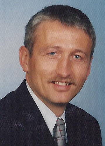 Mittelälterlicher Mann mit Schnurrbart im Anzug, der vor neutralem Hintergrund freundlich in die Kamera lächelt