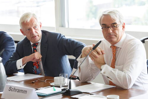 Zwei Geschäftsleute im Konferenzraum diskutieren angeregt neben Mikrofonen und Unterlagen an einem Besprechungstisch