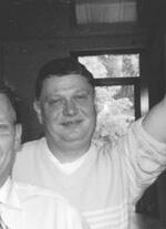 Lächelnder Mann in einem gestreiften Pullover hebt fröhlich den Arm in einem Innenraum mit Fenster im Hintergrund