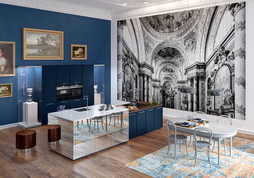 Modern eingerichtete Küche mit blauen Schränken, spiegelnder Kochinsel und Esstisch auf buntem Teppich vor einer großen Wand mit schwarz-weißer Barockfresko-Tapete und gerahmten Gemälden.