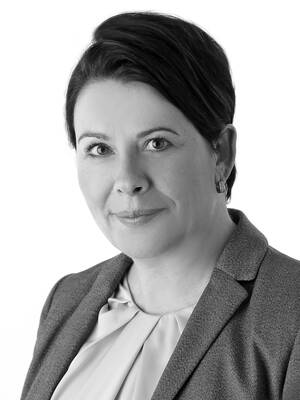 Porträt einer Frau im Business-Outfit mit kurzem dunklem Haar, die in die Kamera blickt und leicht lächelt