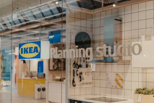 Innenansicht eines IKEA Planning Studios mit moderner Küchenplanung, Wandfliesen, Hängeutensilien und sichtbarem IKEA-Leuchtschild am Glas.