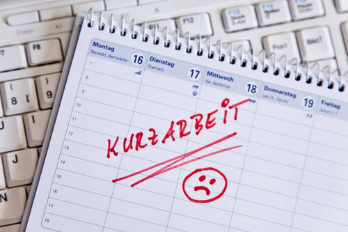 Aufgeschlagener Terminkalender auf einer Computertastatur mit rotem handschriftlichem Eintrag „Kurzarbeit“ und traurigem Smiley am Dienstag, dem 17.