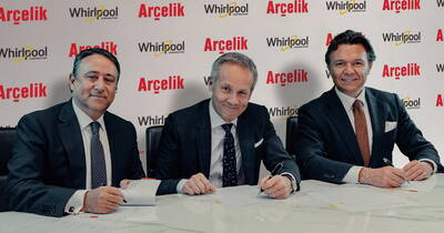Drei Geschäftsleute in Anzügen sitzen an einem Konferenztisch und unterzeichnen lächelnd offizielle Dokumente vor einer Hintergrundwand mit den Logos von Arçelik und Whirlpool.