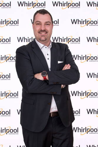 Geschäftsmann im dunklen Anzug mit verschränkten Armen lächelt vor einer Whirlpool-Corporation-Pressewand