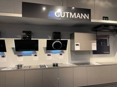 Moderne Küchenausstellung mit GUTMANN-Dunstabzugshauben in Schwarz, beleuchtetem Runddesign und grauen Unterschränken vor hellgrauer Wand mit Informationsblättern