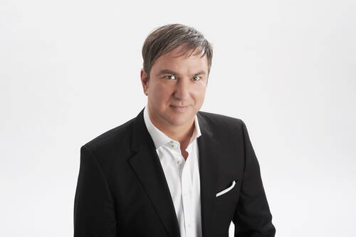 Mittelalterlicher Mann im schwarzen Business-Anzug mit weißem Hemd lächelt freundlich vor hellem, neutralem Hintergrund