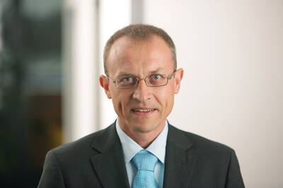 Geschäftsmann mittleren Alters mit Brille und blauem Anzug, der in heller Büro-Umgebung direkt in die Kamera lächelt