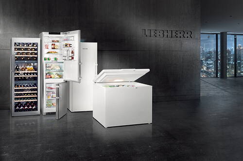 Moderne Loftküche mit geöffneter Kühl-Gefrierkombination, großem Gefrierschrank und beleuchtetem Weinkühlschrank der Marke Liebherr vor dunkler Betonwand und Stadtpanorama im Hintergrund