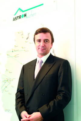 Geschäftsmann im dunklen Anzug steht vor einer Wandkarte mit dem Logo „ASTROH Kuchen“ im Hintergrund.