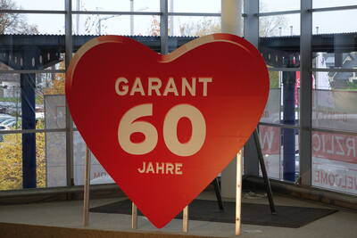 Großes rotes Herzschild mit der Aufschrift „Garant 60 Jahre“ steht als Jubiläumsdekoration in einer verglasten Eingangshalle