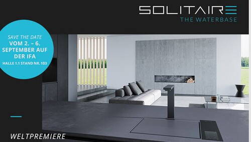 Modern minimalistische Kücheninsel mit integriertem Wasserhahn-System „Solitaire – The Waterbase“ in einem offenen Wohnraum mit grauer Betonwand und Designsofa, beworben als Weltpremiere zur IFA im September.