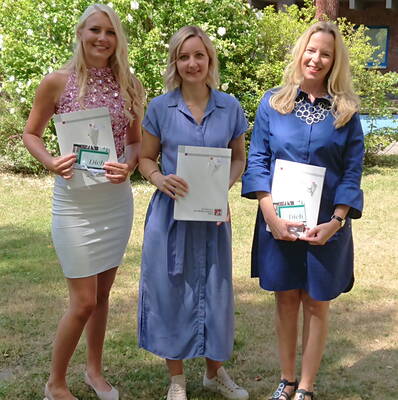 Drei lächelnde Frauen stehen im sommerlichen Garten nebeneinander und halten Urkunden und Glückwunschkarten in den Händen.