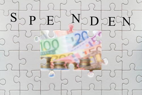 Weiße Puzzlefläche mit dem Wort „Spenden“, in deren mittlerer Lücke unscharf bunte Euro-Geldscheine und Münzstapel sichtbar werden