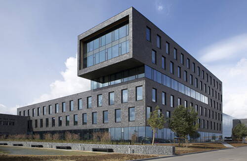 Moderner Bürokomplex aus dunklem Klinker mit großen Glasfronten und auskragendem Obergeschoss an einer begrünten Straße