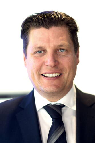 Lächelnder Mann im Anzug mit gestreifter Krawatte vor hellem Hintergrund in einem professionellen Porträtaufnahme.
