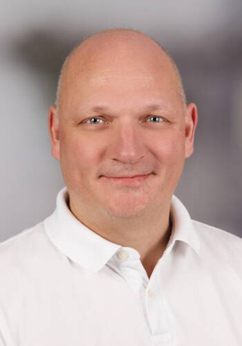 Lächelnder, glatzköpfiger Mann im weißen Poloshirt vor neutral verschwommenem Hintergrund