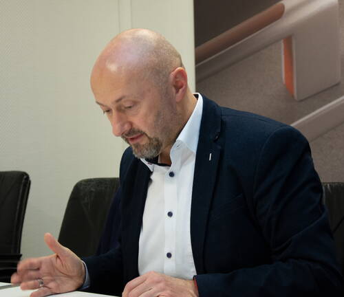 Glatzköpfiger Mann im Anzug sitzt an einem Konferenztisch und spricht konzentriert, während er Notizen oder Unterlagen vor sich betrachtet.
