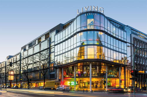 Modernes Einkaufs- und Designzentrum „Living Berlin“ mit großer verglaster Fassade an stark befahrener Straße in der Abenddämmerung
