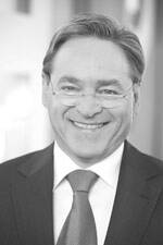 Lächelnder Mann mittleren Alters im Anzug und mit Krawatte in einem schwarz-weißen Porträt vor unscharfem Hintergrund