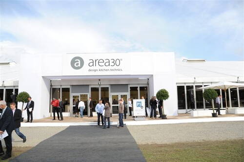 Besucherinnen und Besucher stehen vor dem weißen Messezelt „area30“ für Design, Küche und Technik und unterhalten sich im Eingangsbereich.